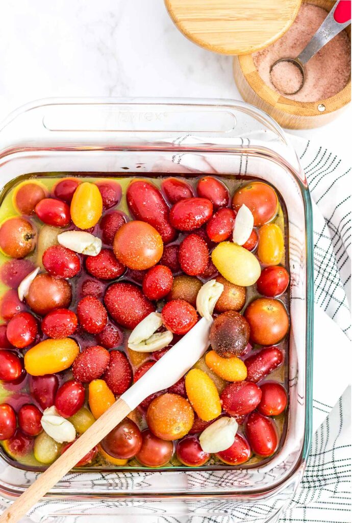 cherry tomatoes and garlic clove covered in olive oil in the baking dish