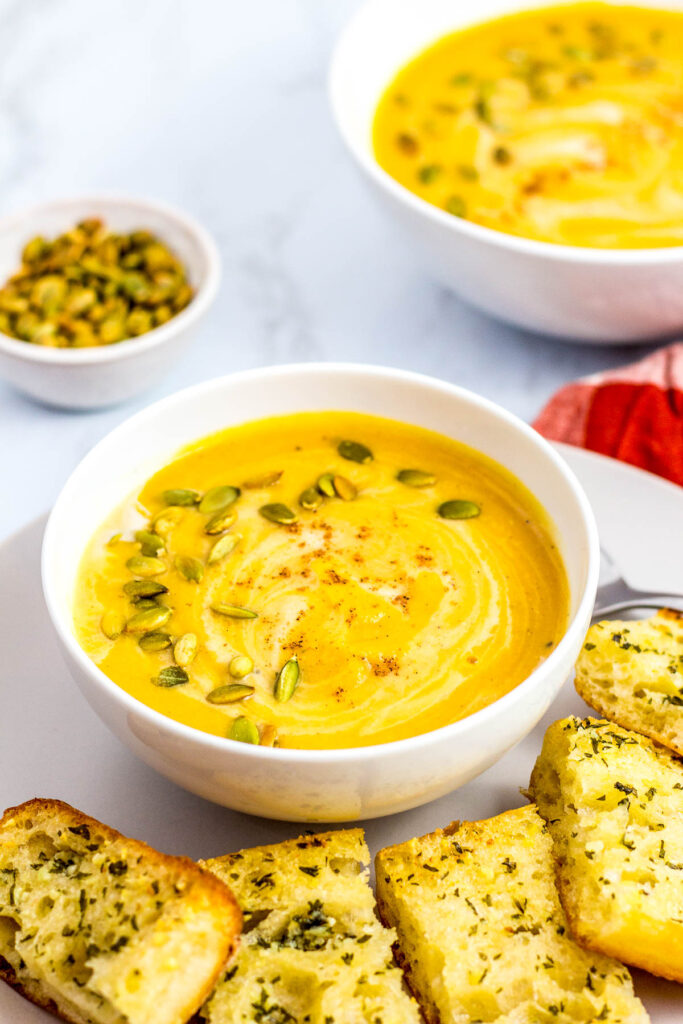 two bowls of butternut squash soup with garlic bread