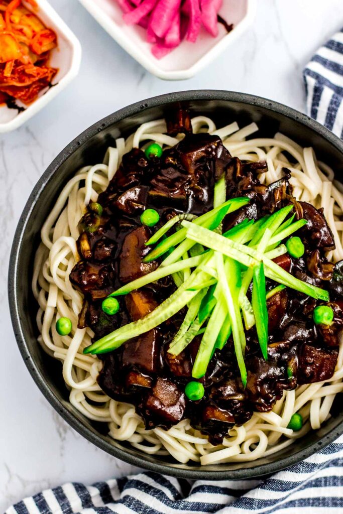 a big bowl of vegan jjajangmyeon with cucumber and pea garnish on top