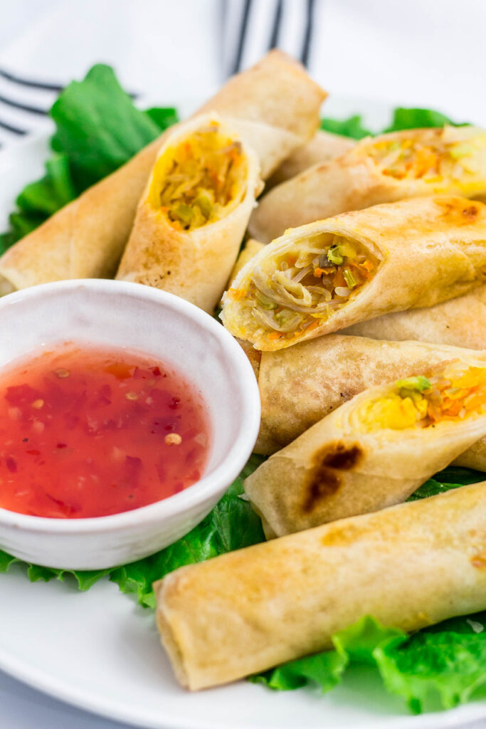 Close up photos of vegan spring rolls (vegan lumpia) - some are cut in half so you can see the vegetable fillings inside