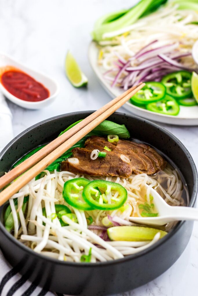 a bowl of pho chay with seitan, bok choy, bean sprouts, jalapeno, onion, and a lime wedge on top.