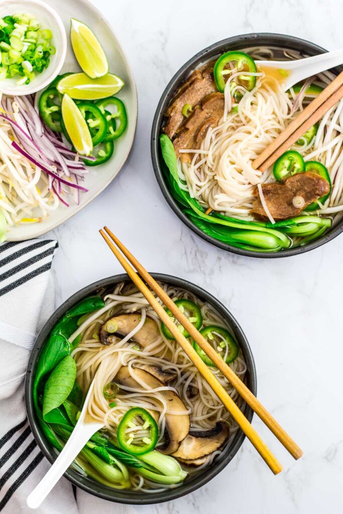 overhead shot of two bowls of vegan pho, one with seitan slices and the other with mushroom