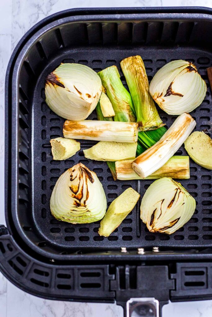 charred onion, green onion, and ginger in an air fryer basket