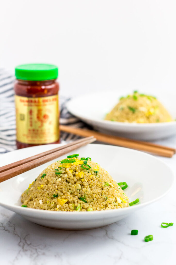 two bowls of healthy egg quinoa fried rice with chili garlic sauce in the background