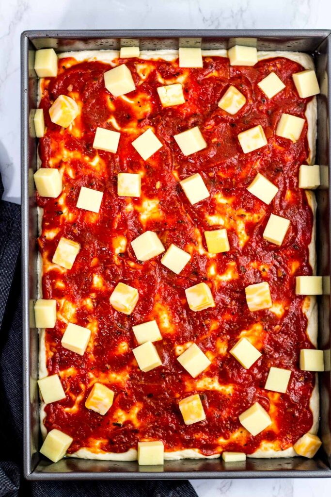 Pizza dough, sauce, and cheese in rectangular baking pan