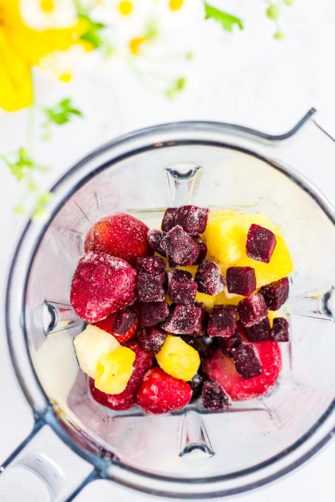 overhead shot of fruits and frozen red beet in the blender before blending