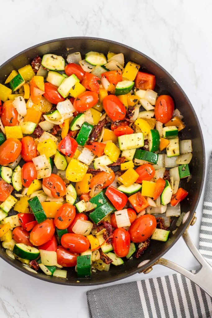 sautéed vegetables (onion, tomato, zucchini, and pepper) in the skillet