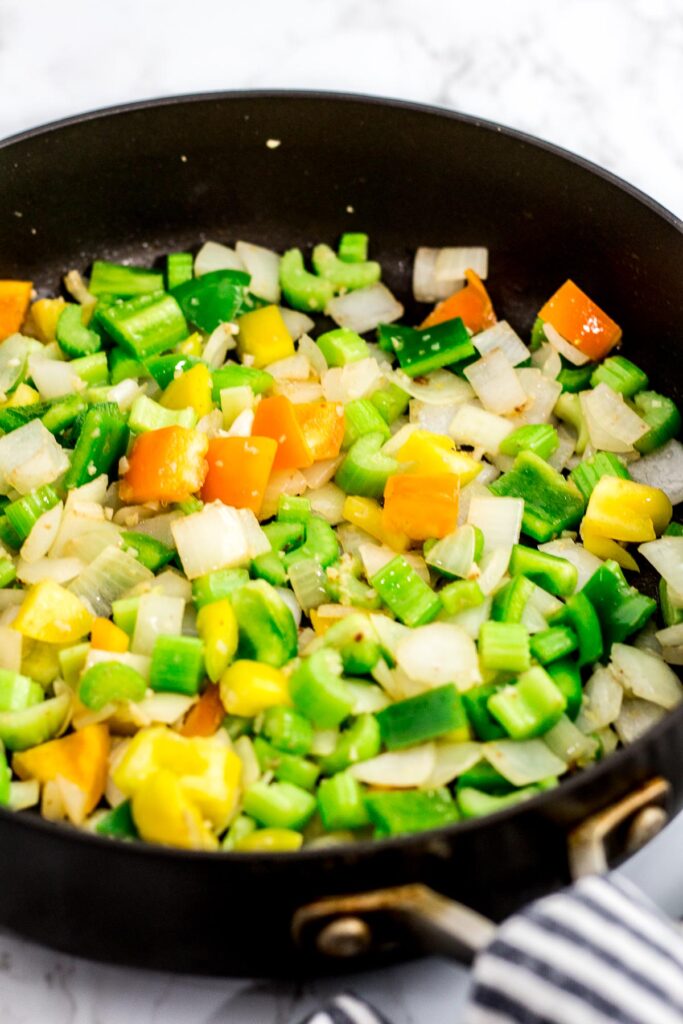 Onion, celery, garlic, and bell pepper being sautéed in the pan