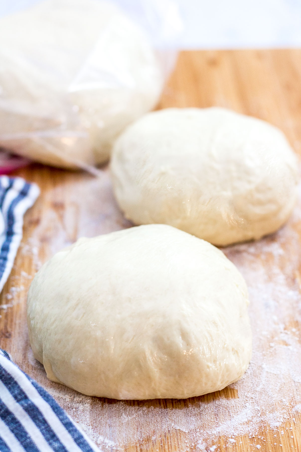 one pizza dough in a freezer bag and two smaller pizza dough on a cutting board