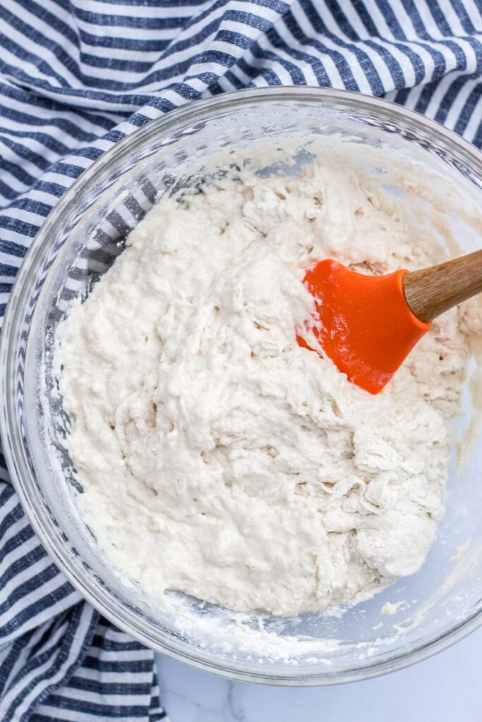 Mixture of flour, salt, and bloomed yeast mixture mixed in a bowl with a rubber spatula