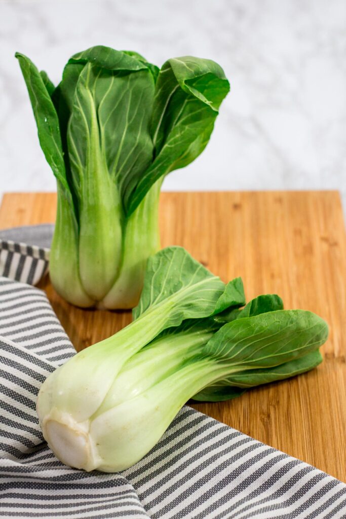 two unwashed bok choy on a wooden cutting board