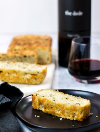 sliced small batch garlic green onion focaccia with a glass of red wine in the background
