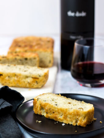 sliced small batch garlic green onion focaccia with a glass of red wine in the background