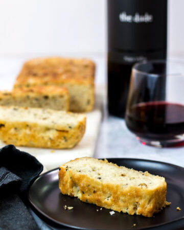 sliced small batch garlic green onion focaccia with a glass of red wine in the background