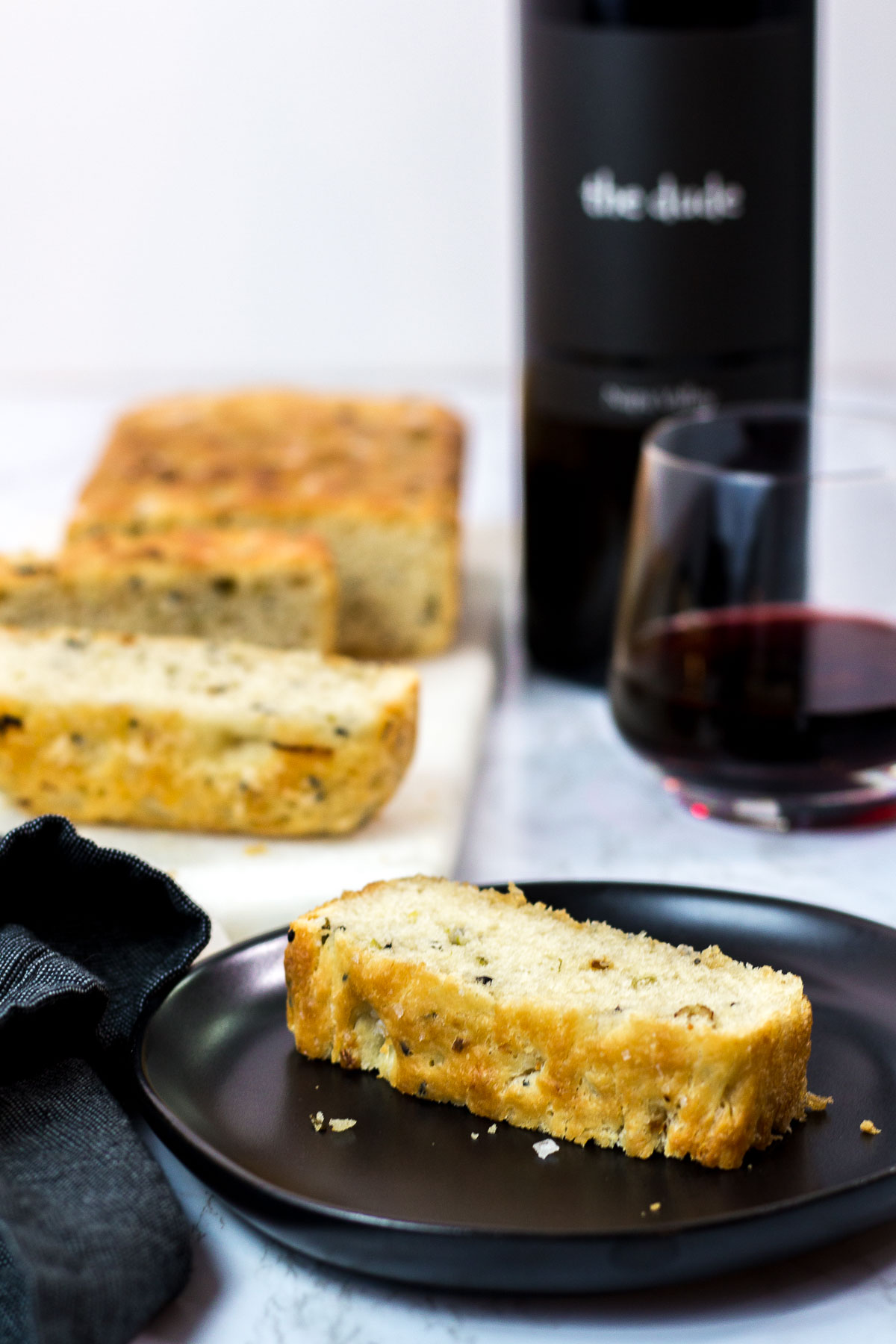 sliced small batch garlic green onion focaccia with a glass of red wine in the background