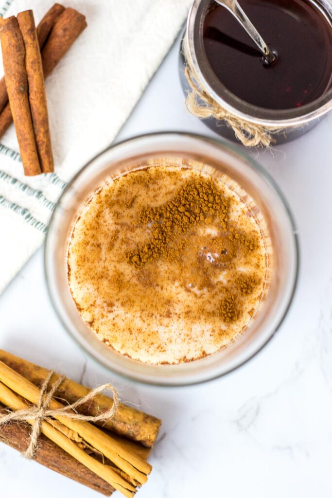 overhead shot of cinnamon syrup, cinnamon powder, and oatmilk in a glass