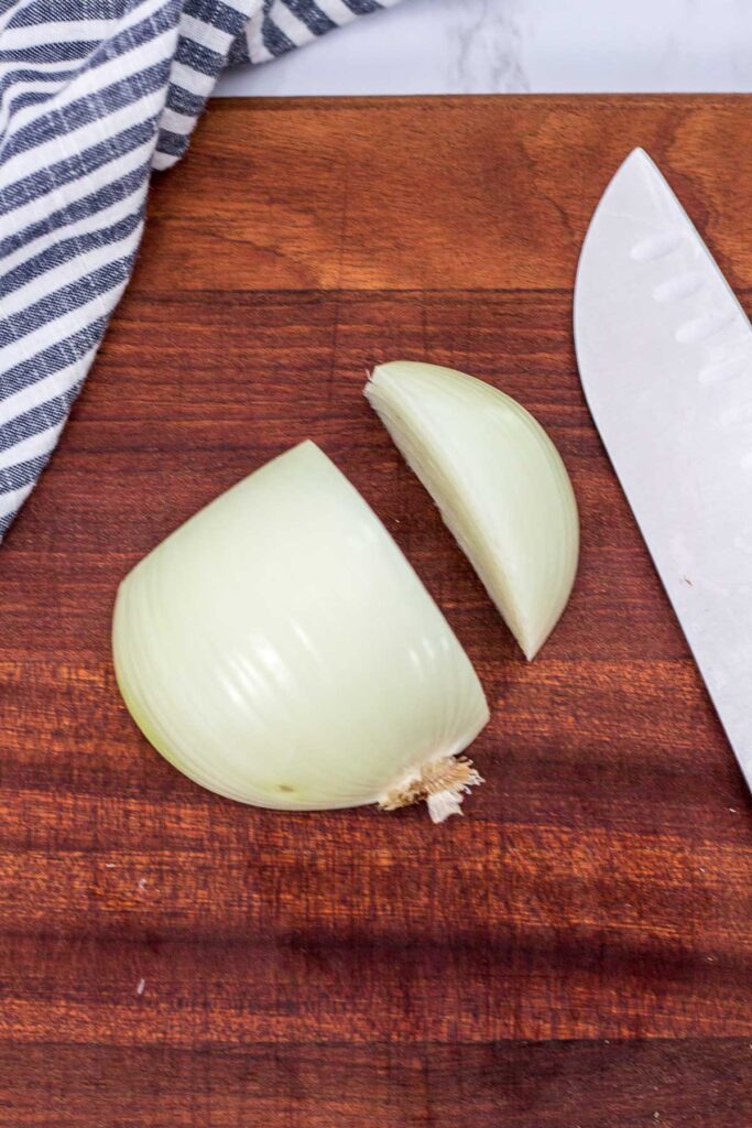 half of a peeled onion on a wooden cutting board, small chunk of onion ready to be minced