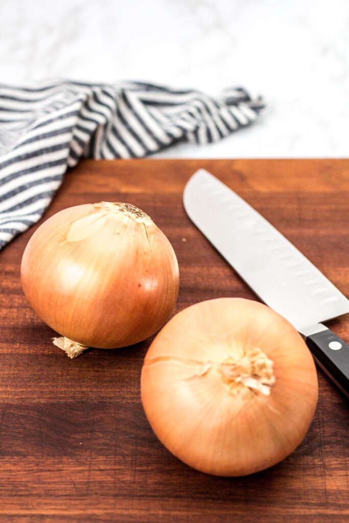 two large yellow onions on a cutting board with a chef knife