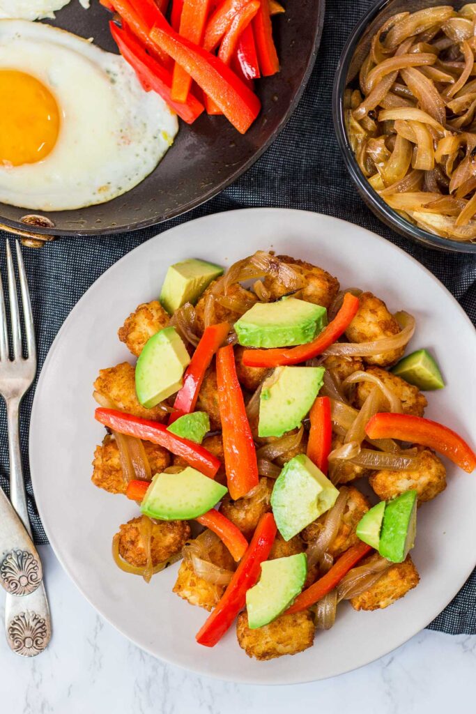 air fried tater tots, avocado, caramelized onion, and sauteed peppers on a plate