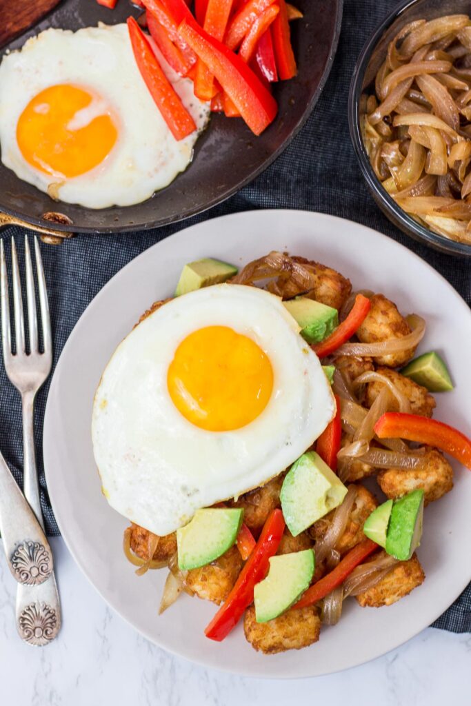 tater tots, pepper, onion, avocado, and an egg on a plate