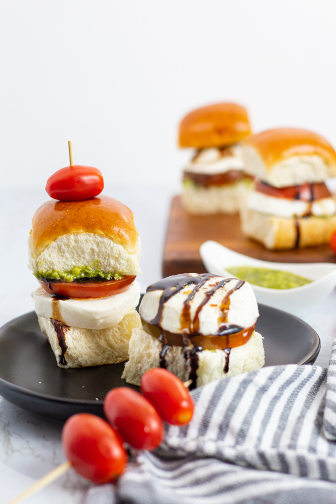 two caprese sliders on a plate and two more sliders in the background