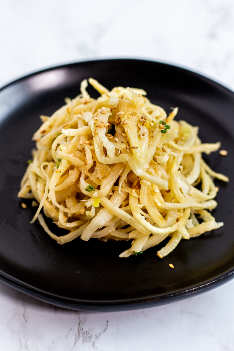 sauteed bellflower roots (doraji namul) on a black plate, garnished with sesame seeds