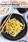 sauteed doraji on a black plate with chopsticks next to it