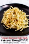 close up photo of sauteed doraji garnished with sesame seeds on a black plate