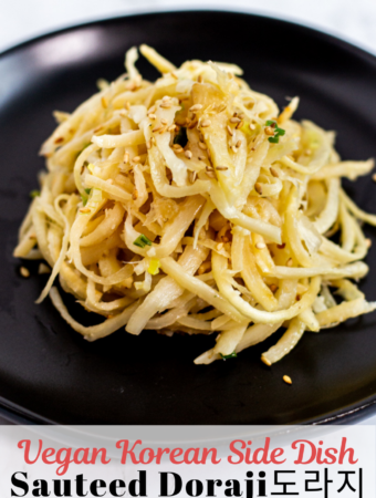 close up photo of sauteed doraji garnished with sesame seeds on a black plate