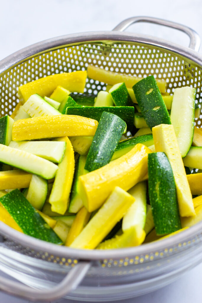 cut zucchini and yellow squash strips in a colander with sprinkle of salt on top.