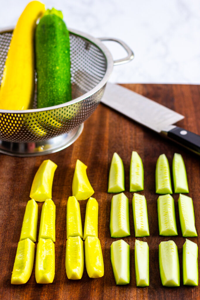 zucchini and yellow squash cut into 2-inch strips on a cutting board.