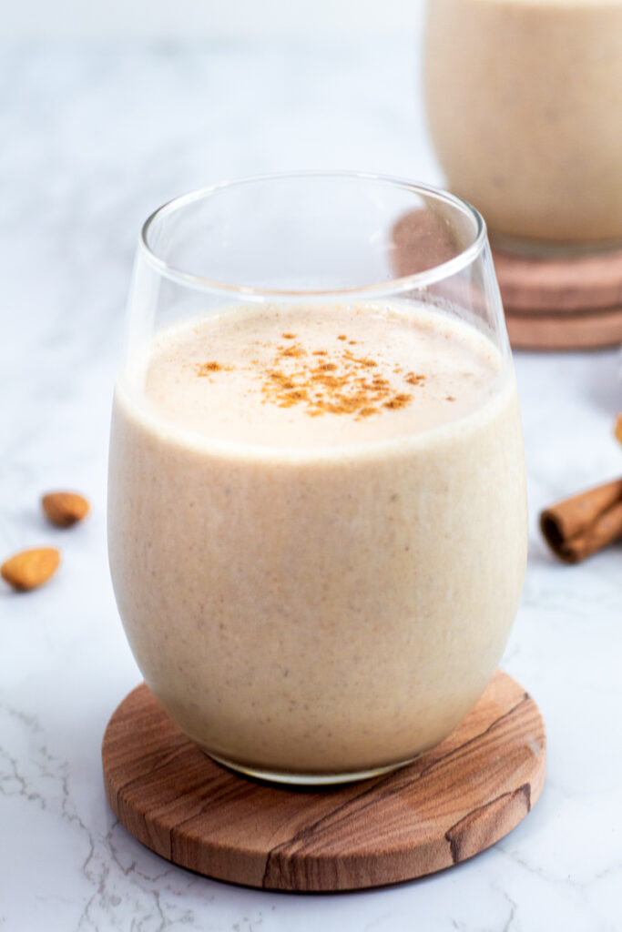 close up photo of almond butter smoothie with banana in a clear glass and sprinkle of cinnamon on top.