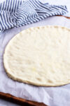 flatten circular pizza dough on the parchment paper.