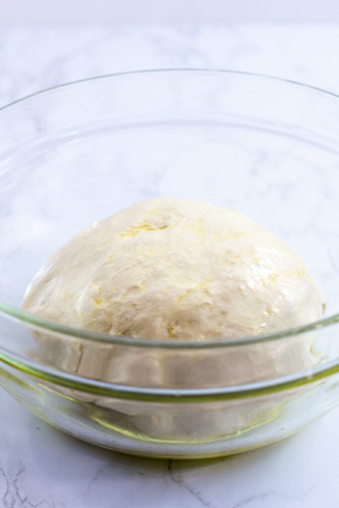 pizza dough covered in olive oil in a clear bowl before rising.