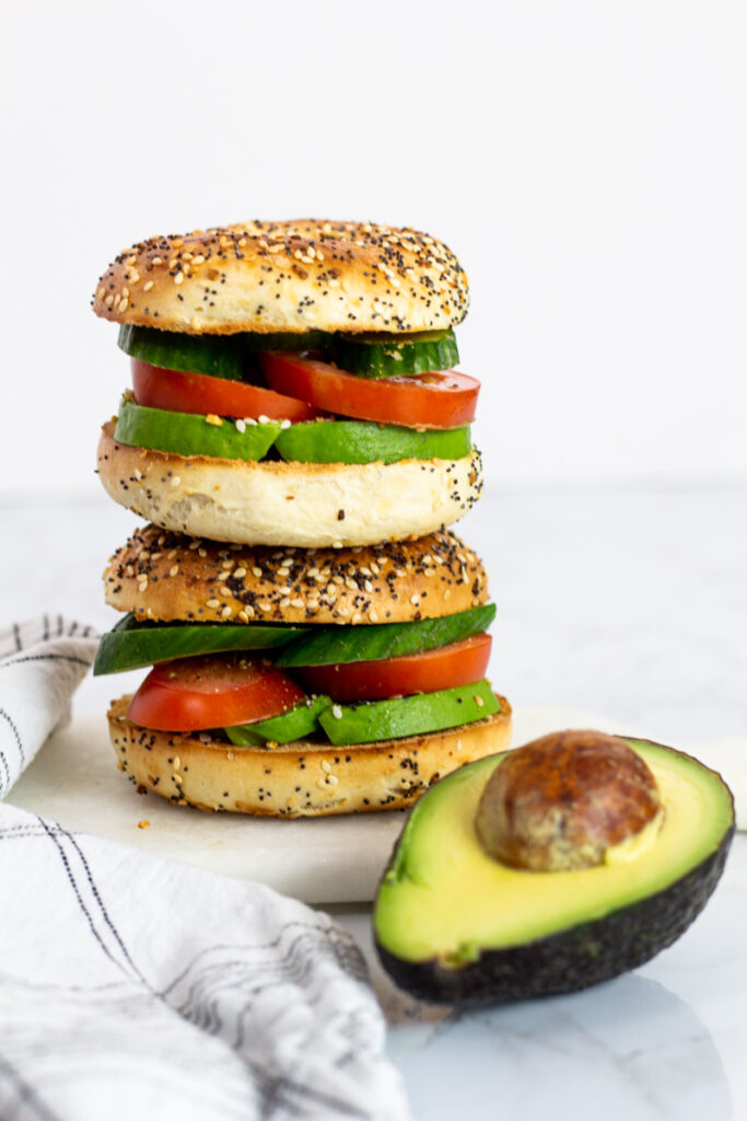 two avocado bagel sandwiches stacked on top of each other.