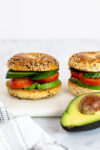 two avocado bagel sandwich on a white board.