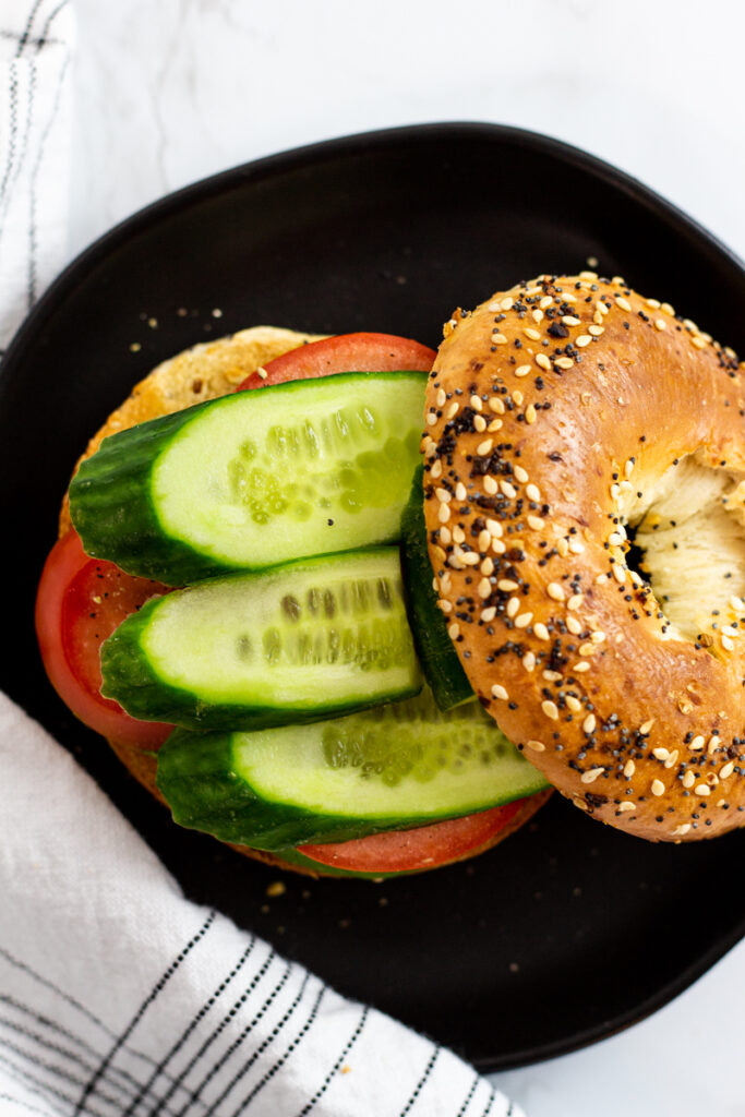 overhead shot of bagel sandwich with cucumber slices on the top of tomato and avocado.