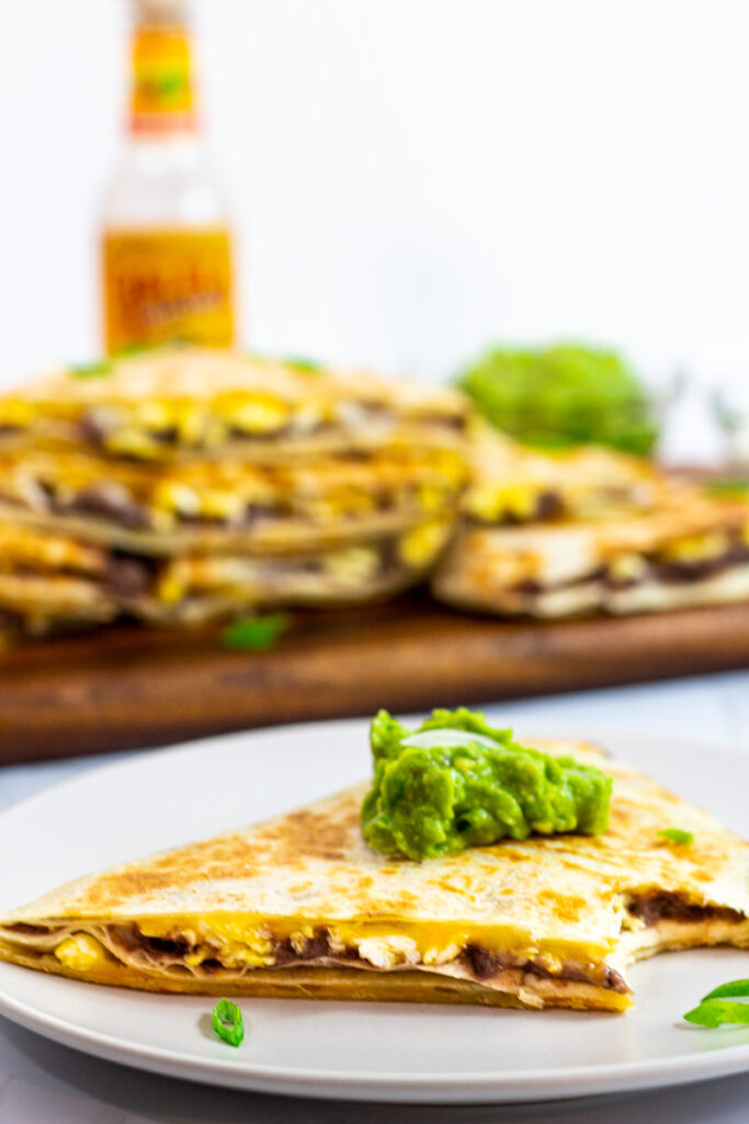 A piece of breakfast quesadilla with refried beans and eggs with a dollop of guacamole on top.