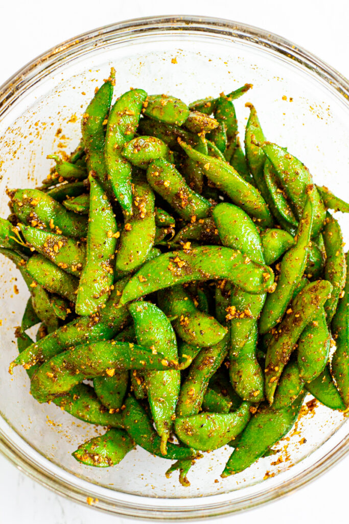 spicy edamame coated with seafood garlic butter in a clear bowl.