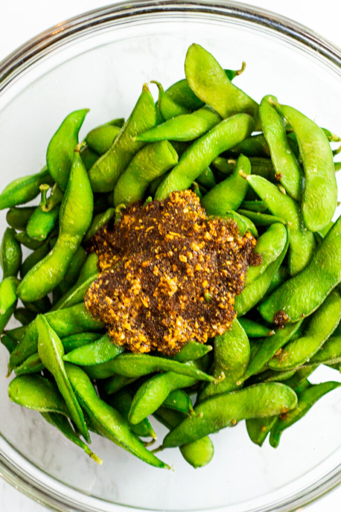 the seafood garlic butter sauce is poured over cooked edamame in a clear bowl.