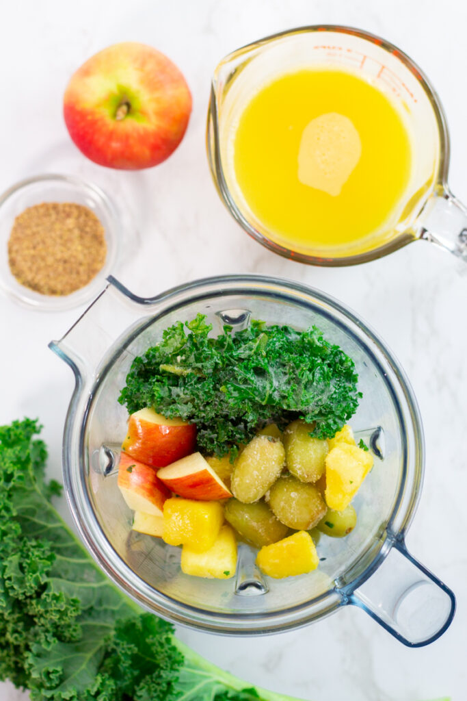 apple, frozen kale, grape, and pineapple in the blender with orange juice on the side.