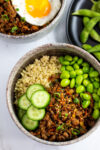 overhead shot of vegan buddha bowl with quinoa, vegan bulgogi, edamame, and cucumber slices.