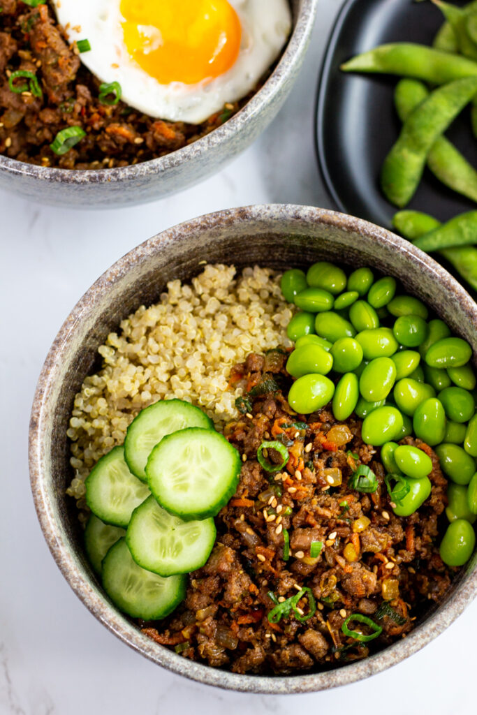 overhead shot of vegan buddha bowl with quinoa, vegan bulgogi, edamame, and cucumber slices.