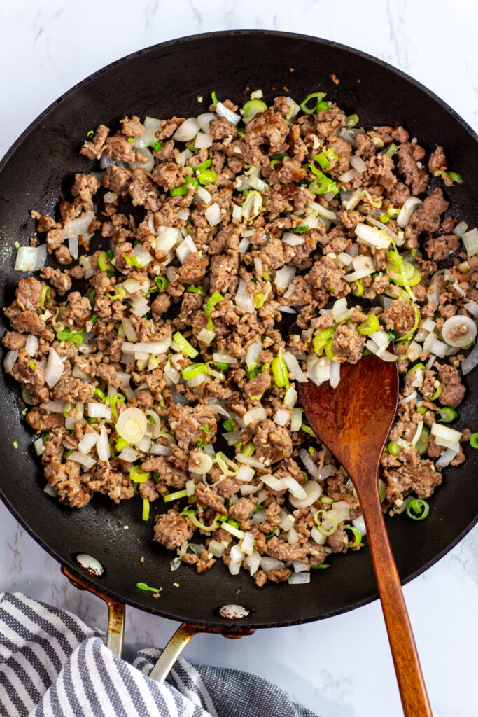 cooked impossible meat with green onion and onion in the pan.