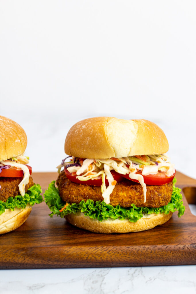 two vegan chicken sandwiches with pepper jelly coleslaw on a wooden board.