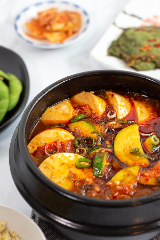 Vegan soondubu jjigae photo on an angle with other side dishes in the background.