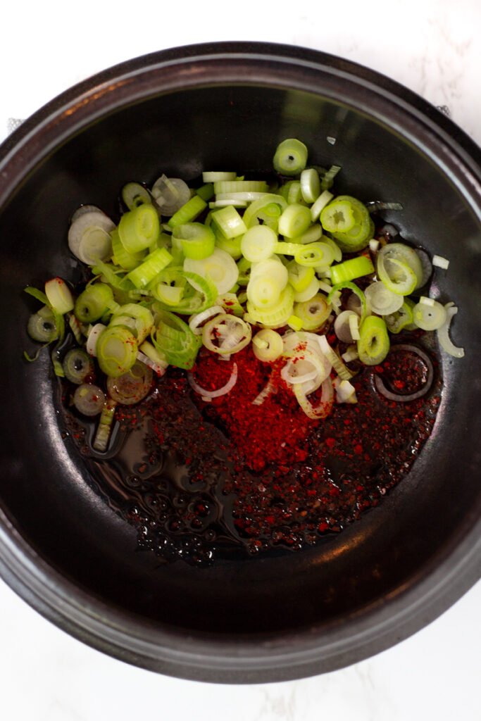 White parts of green onion, oil, and Korean red pepper flakes in a Korean clay pot.