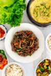 Over-head shot of Korean BBQ beef bulgogi, lettuce, steamed egg, rice, cucumber kimchi, and vegetables.