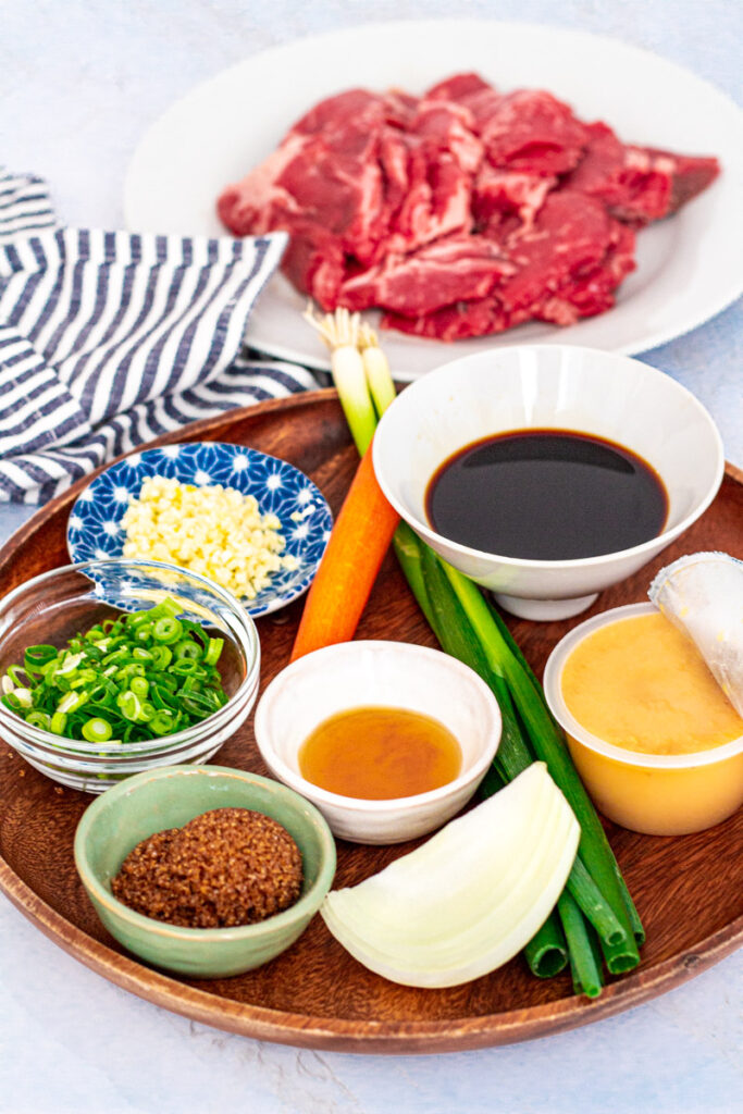 Marinade ingredients - sliced beef, soy sauce, apple sauce, green onion, onion, sesame oil, brown sugar, minced garlic, and carrots.