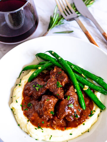 Overhead shot of brandy braised beef on the bed of mashed potato with green beans on the side.